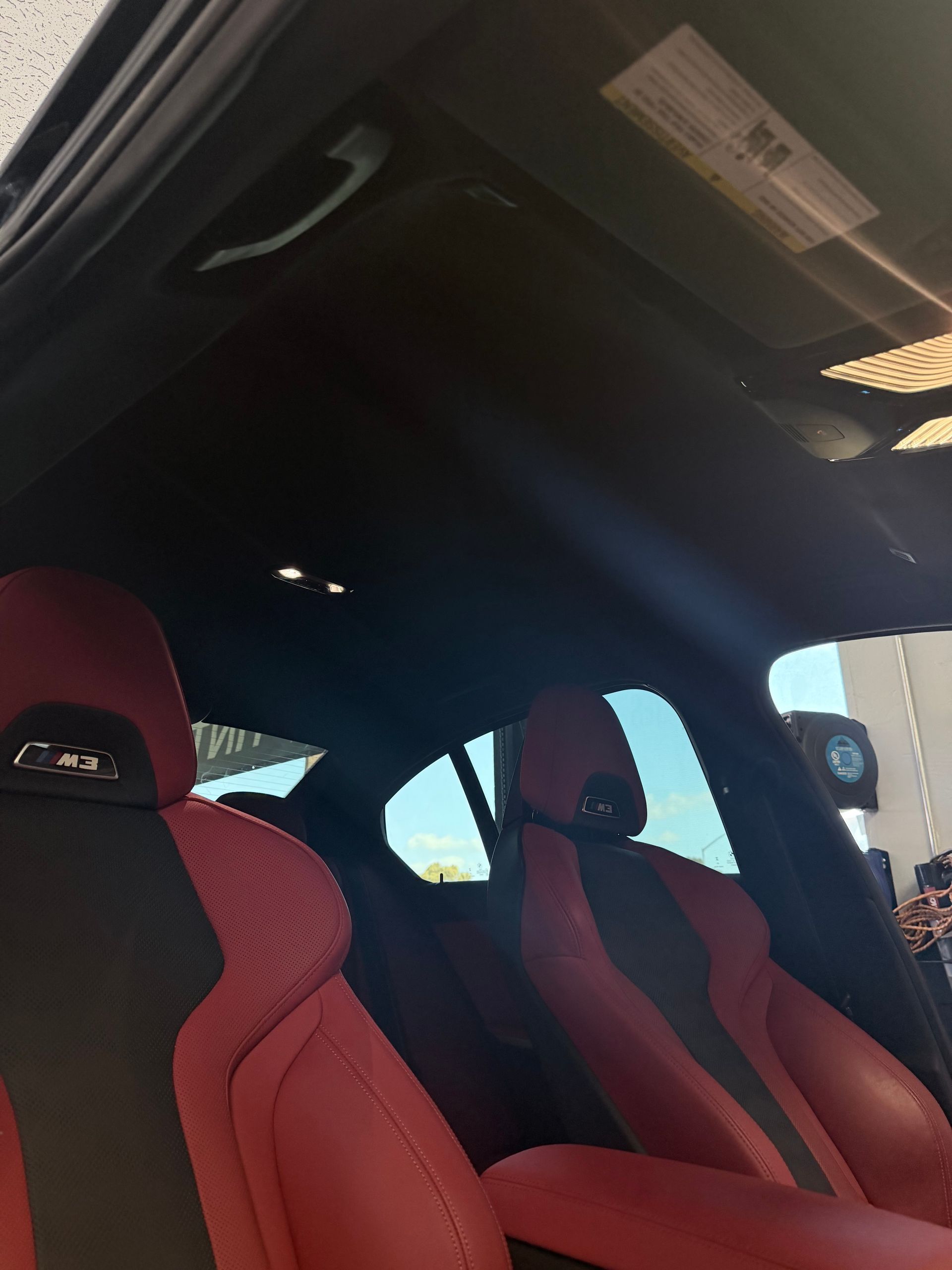 The interior of a vehicle featuring black and red bucket seats with M badges and a black headliner.