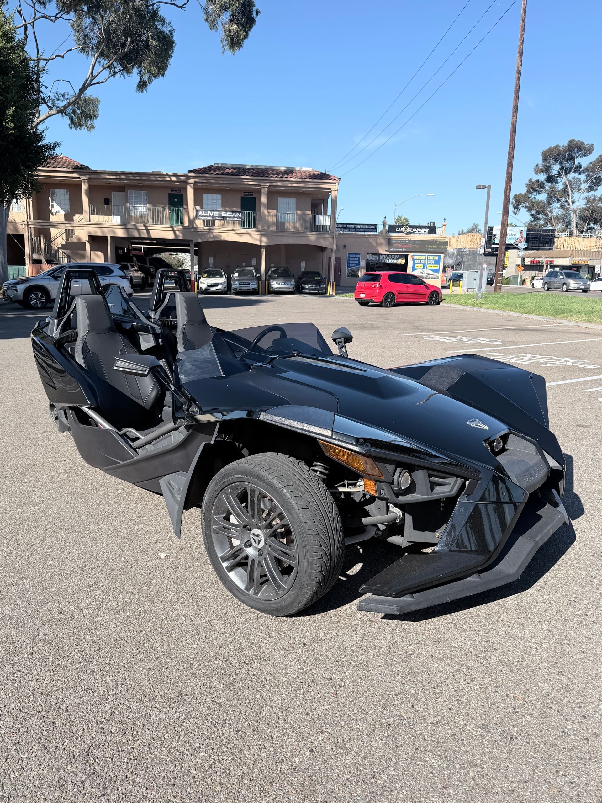 A black Polaris Slingshot three-wheeled autocycle parked in an outdoor gravel lot during the day.