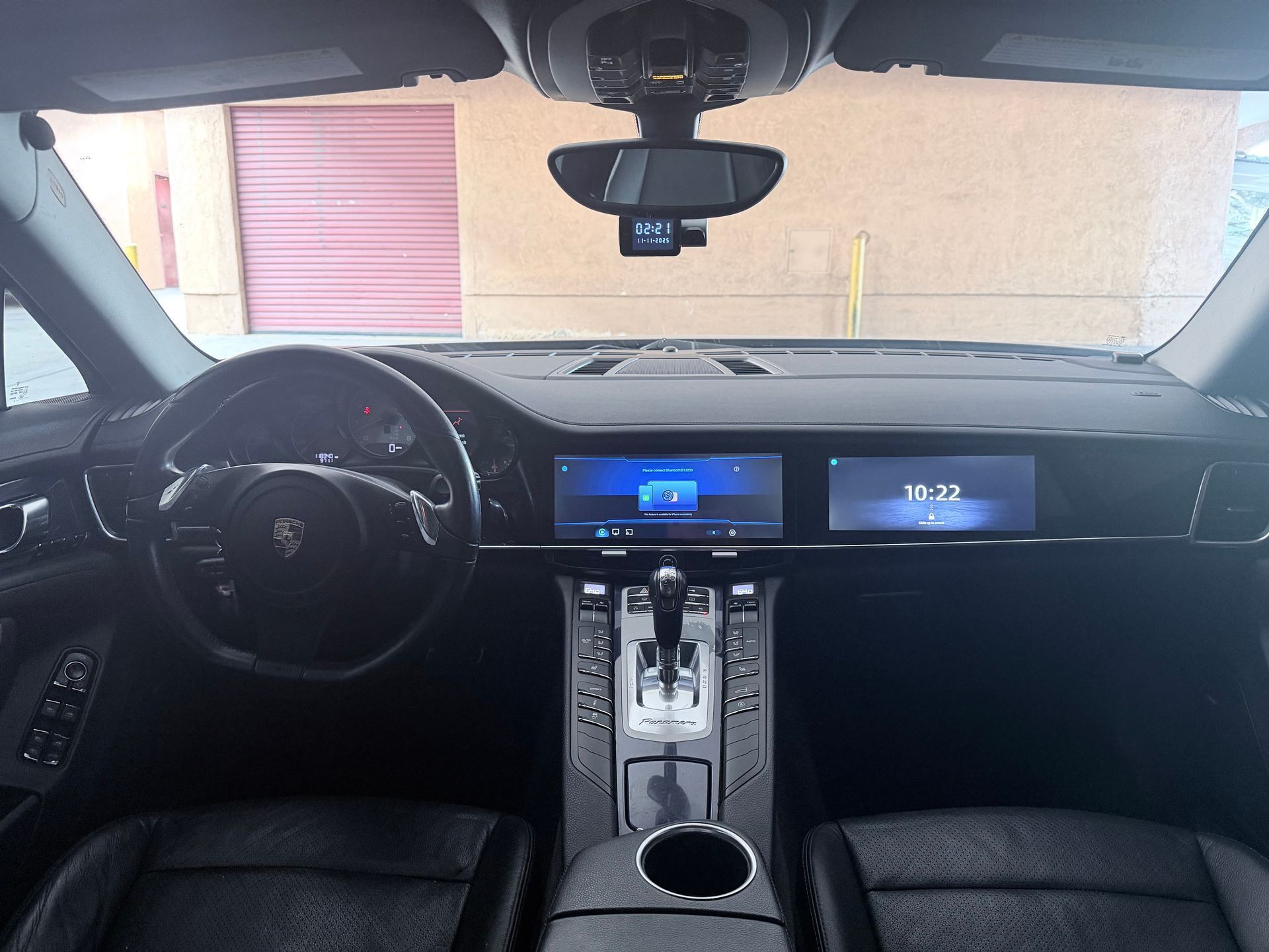 A view from the driver's seat of a black car, showing the steering wheel, digital dashboard displays, and center console.