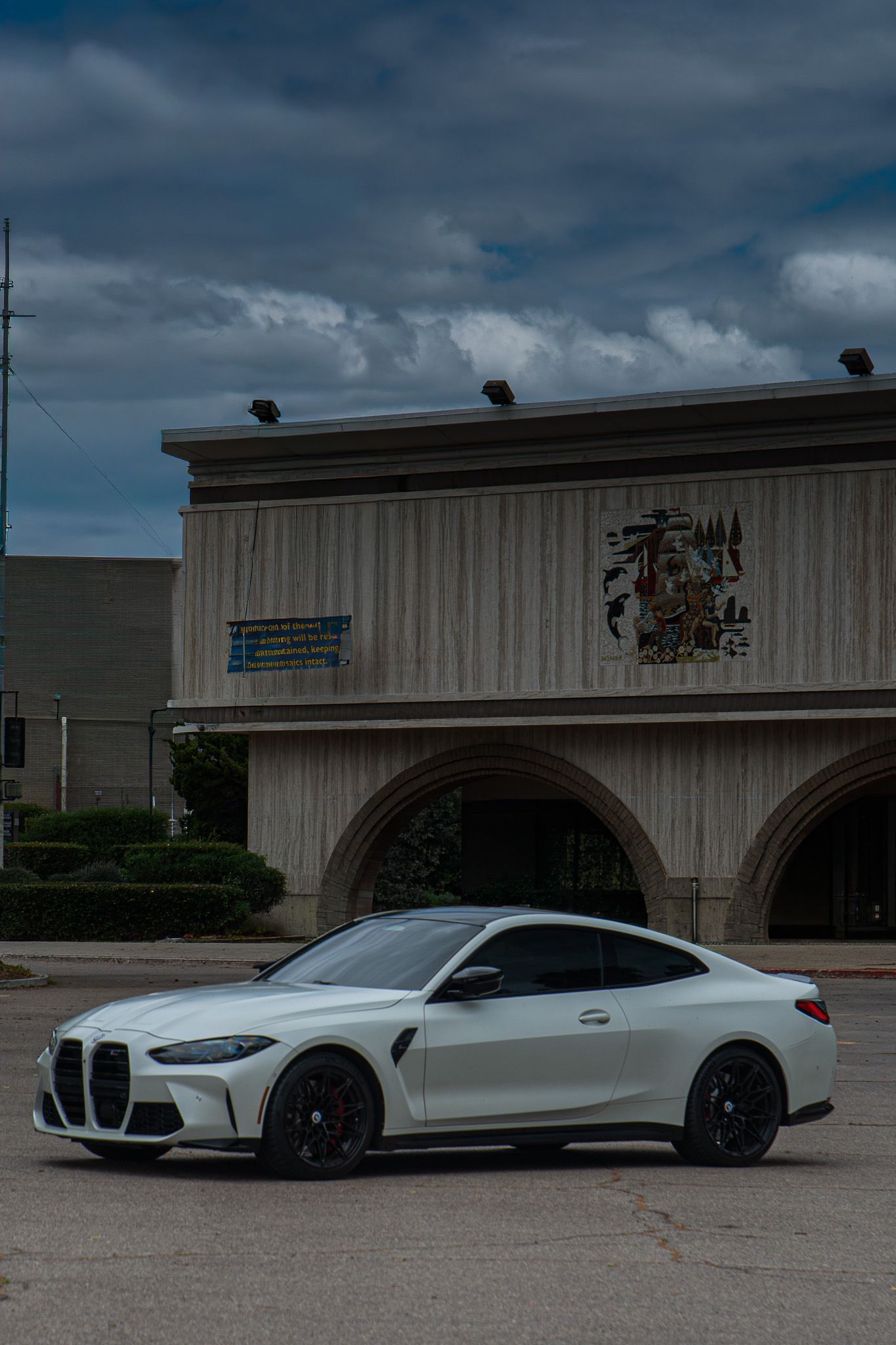White sports coupe parked in front of a stone building under a cloudy sky