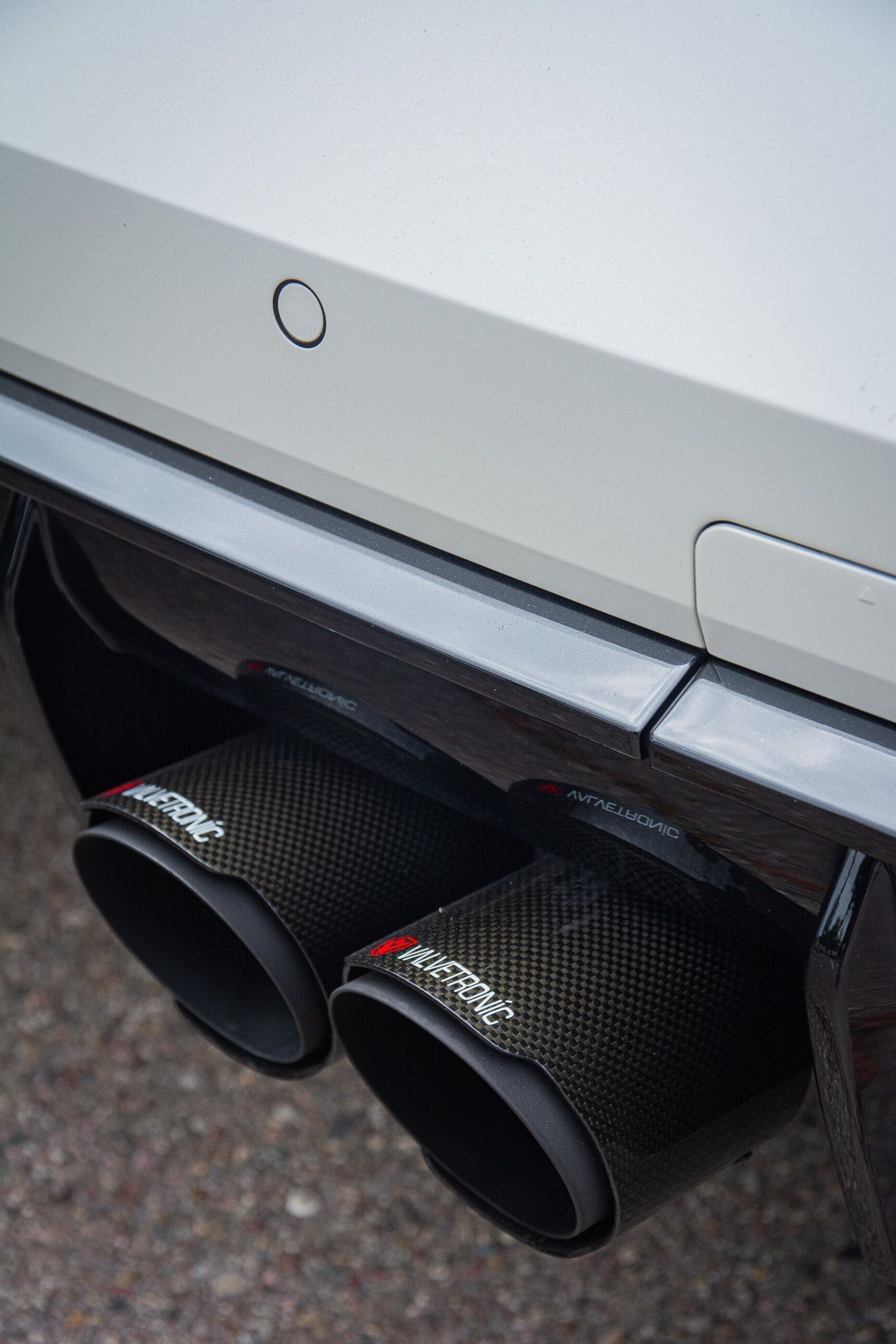 Close-up of a silver car’s rear bumper with two black exhaust tips.