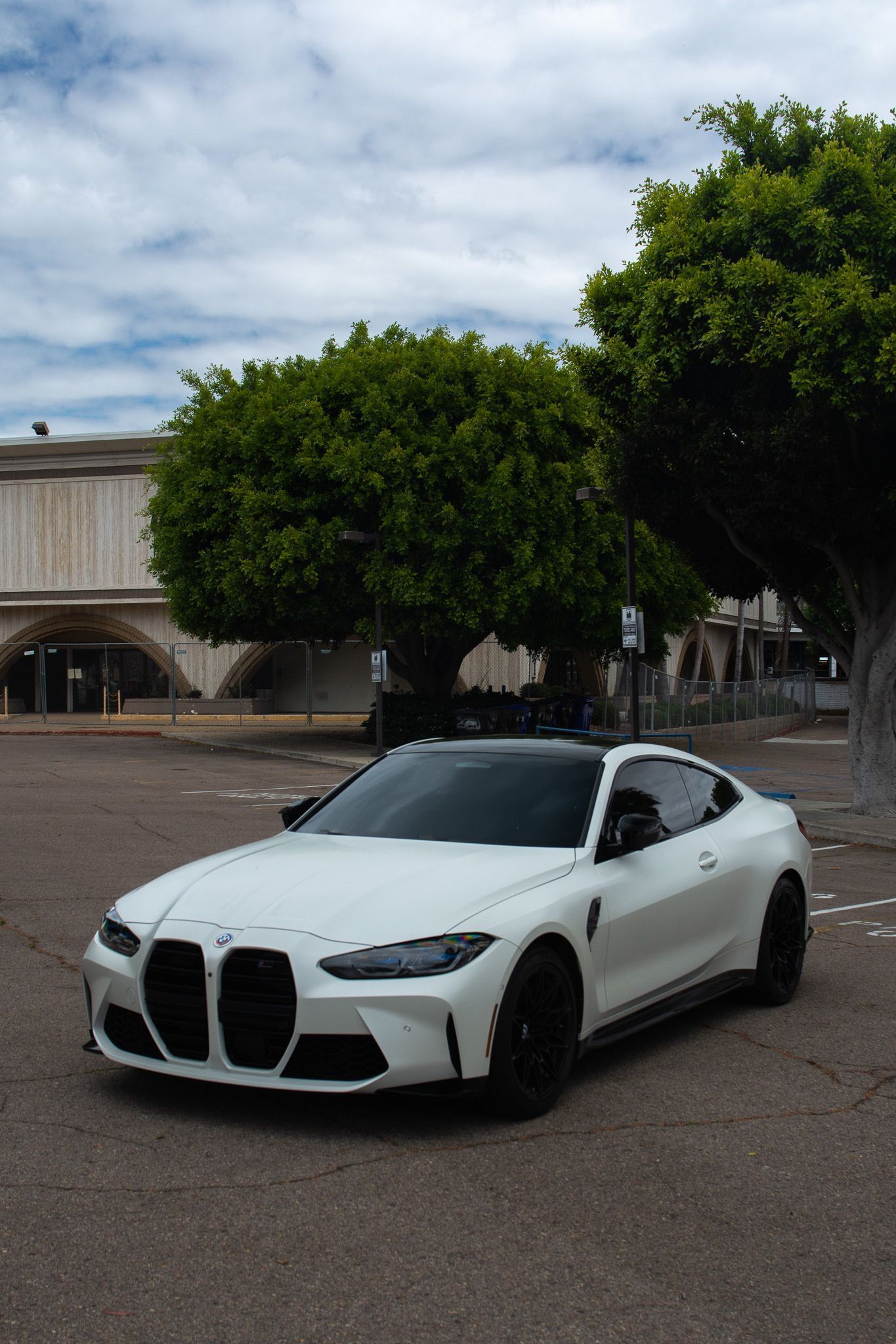 White BMW sports sedan parked on a street with trees and buildings in the background