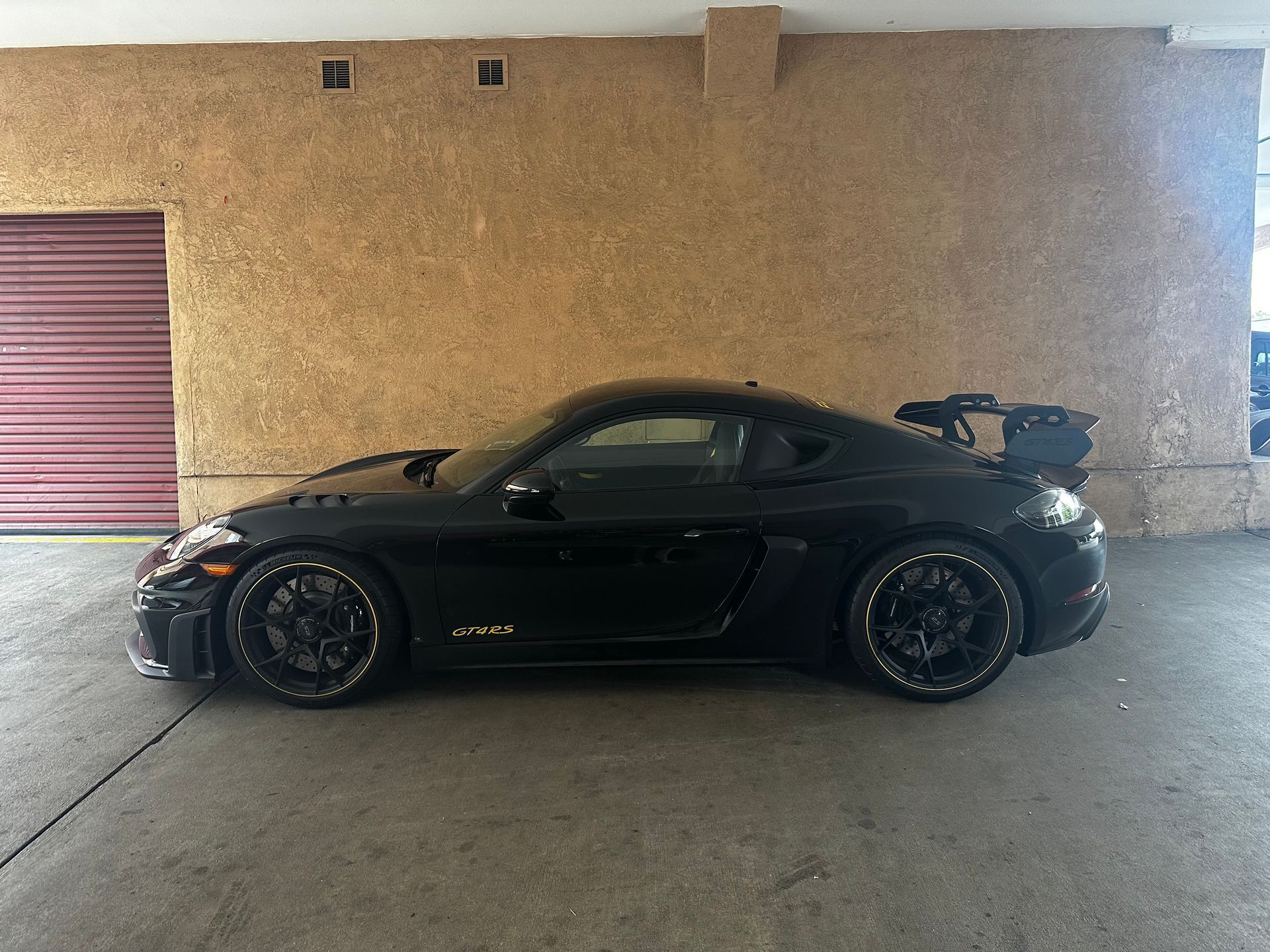 Black sports car parked in a garage with a red door.