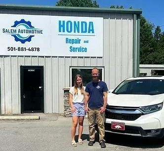 Woman and man stand outside a Honda repair shop next to a white SUV.