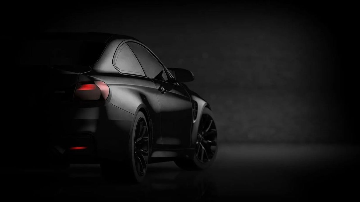Black sports car in a dark setting, taillight illuminated, wheels visible.