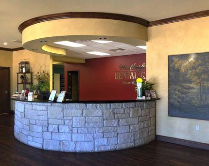 Reception area with stone-faced counter, maroon wall, and logo for a dental clinic.