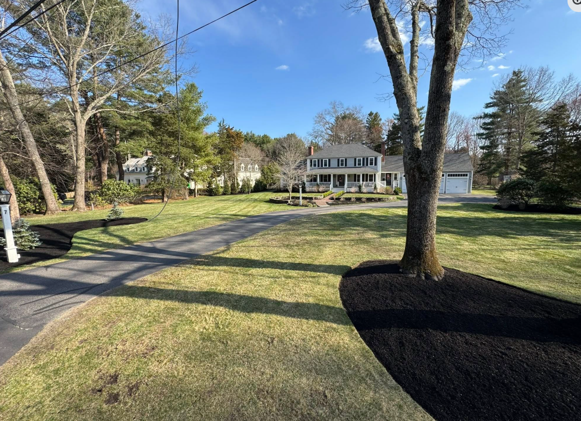 A large house is sitting in the middle of a lush green field surrounded by trees.