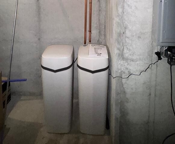 Two white water softener tanks in a basement with exposed pipes and a concrete wall.