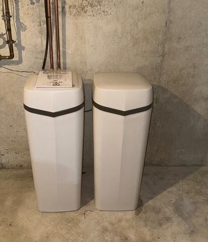 Two white water softener tanks against a concrete basement wall.