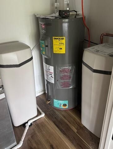 Water heater between two white appliances on a wood floor in a utility room