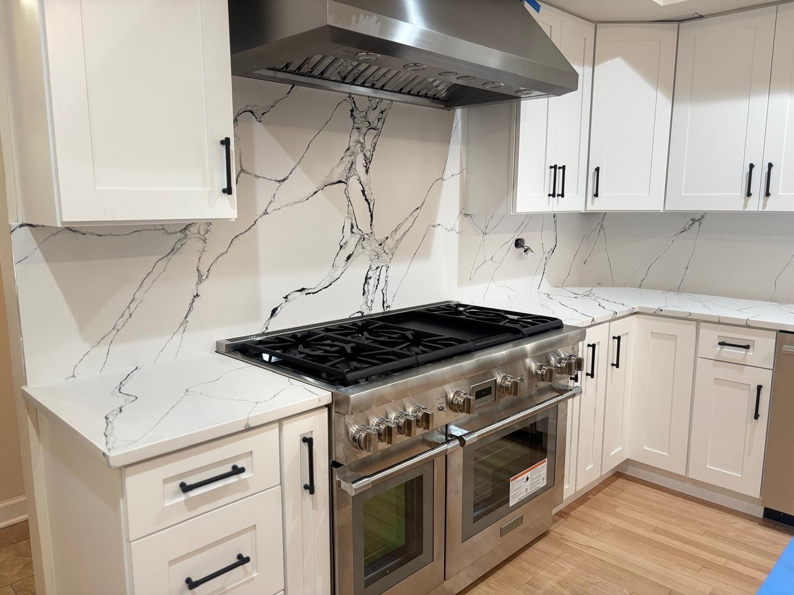 Modern kitchen with stainless steel stove and hood, white cabinets, and marble-look backsplash.
