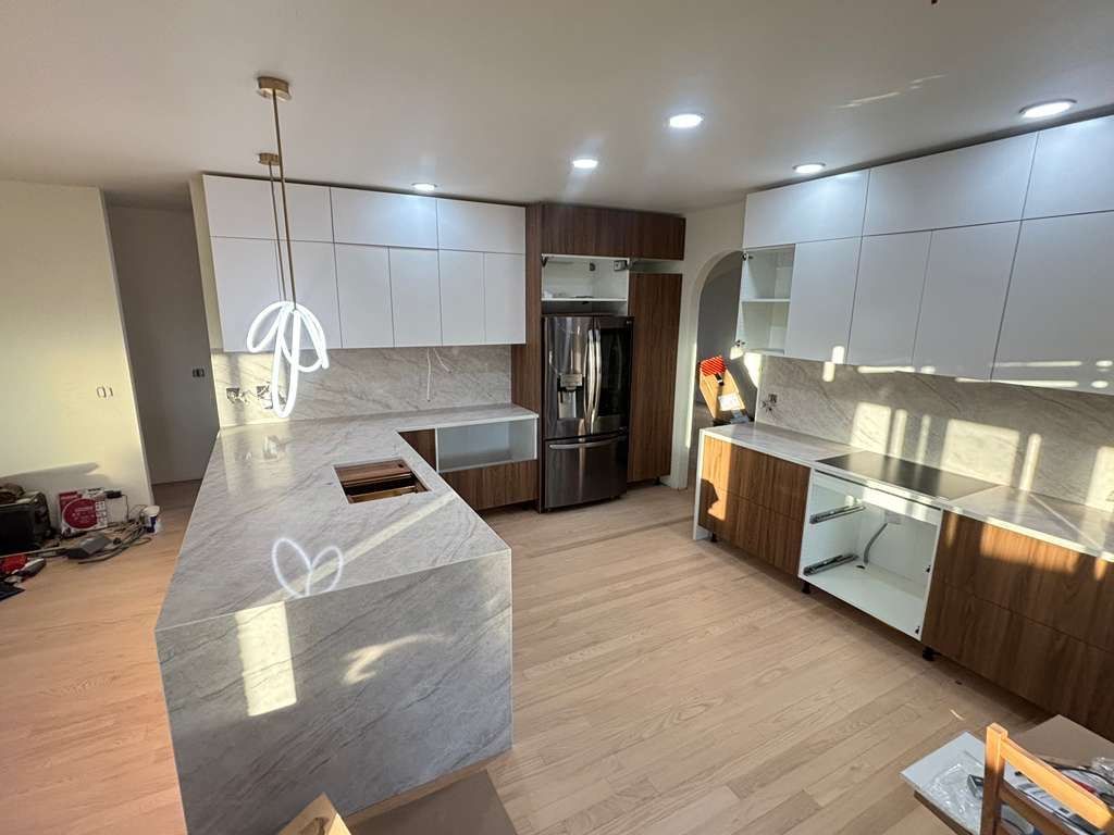 Modern kitchen with white cabinets, wood accents, island, pendant lights, and stainless steel refrigerator