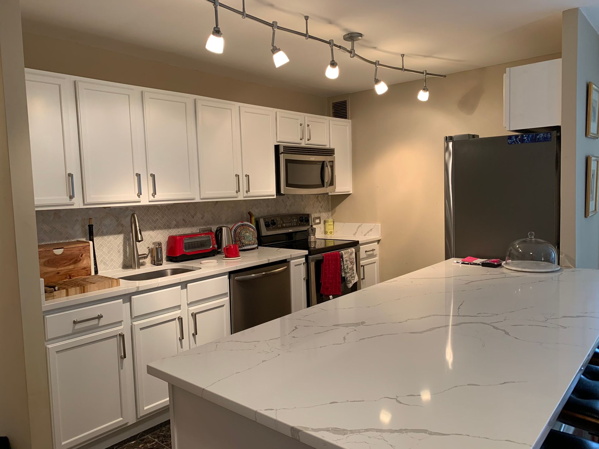 Modern white kitchen with marble island, stainless appliances, and track lighting