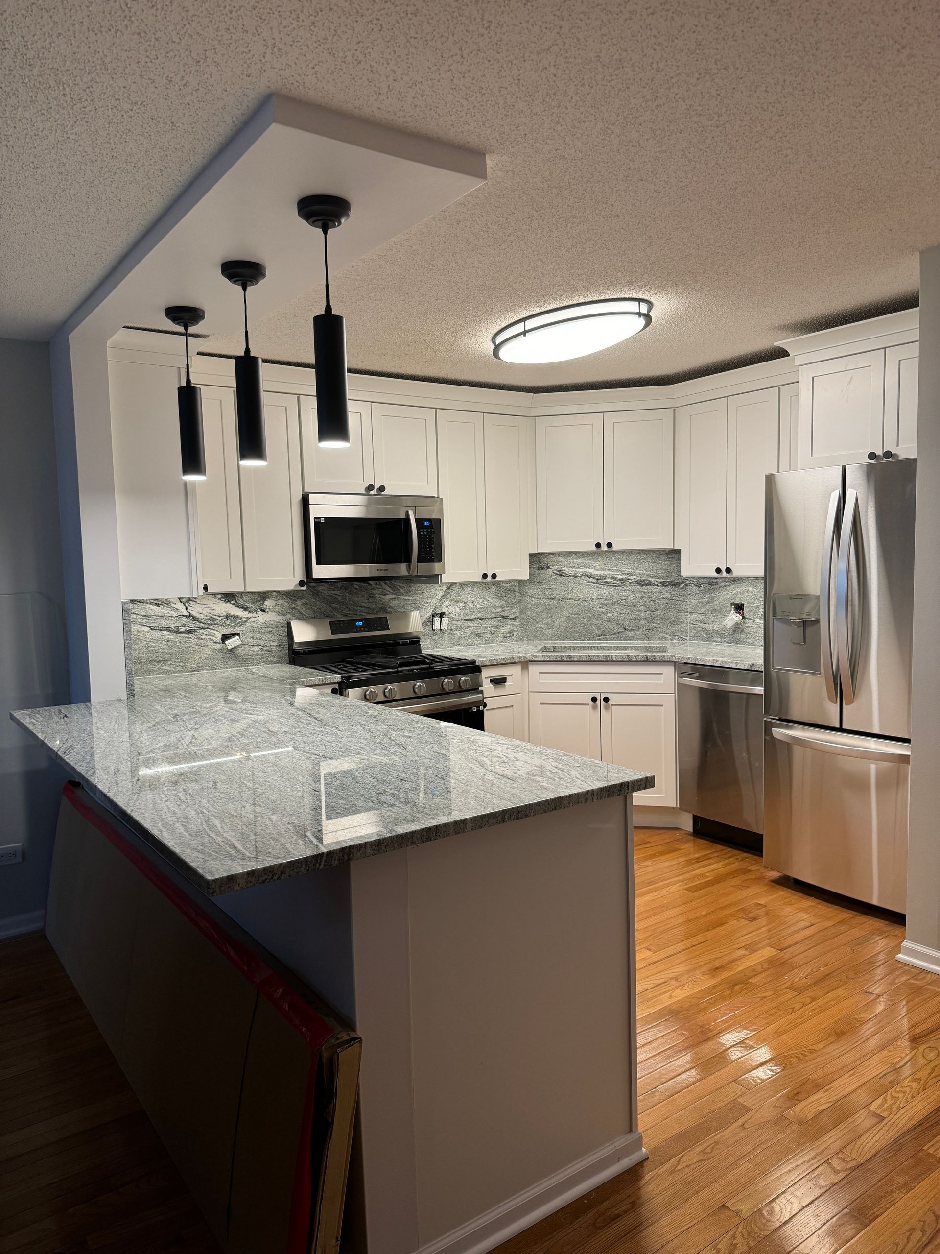 Modern kitchen with white cabinets, granite island, stainless steel appliances, and pendant lights