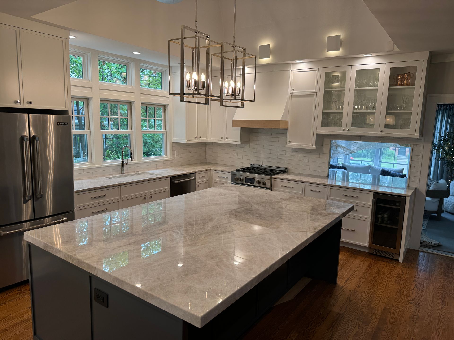 Modern kitchen with large island, stainless fridge, white cabinets, and hardwood floors