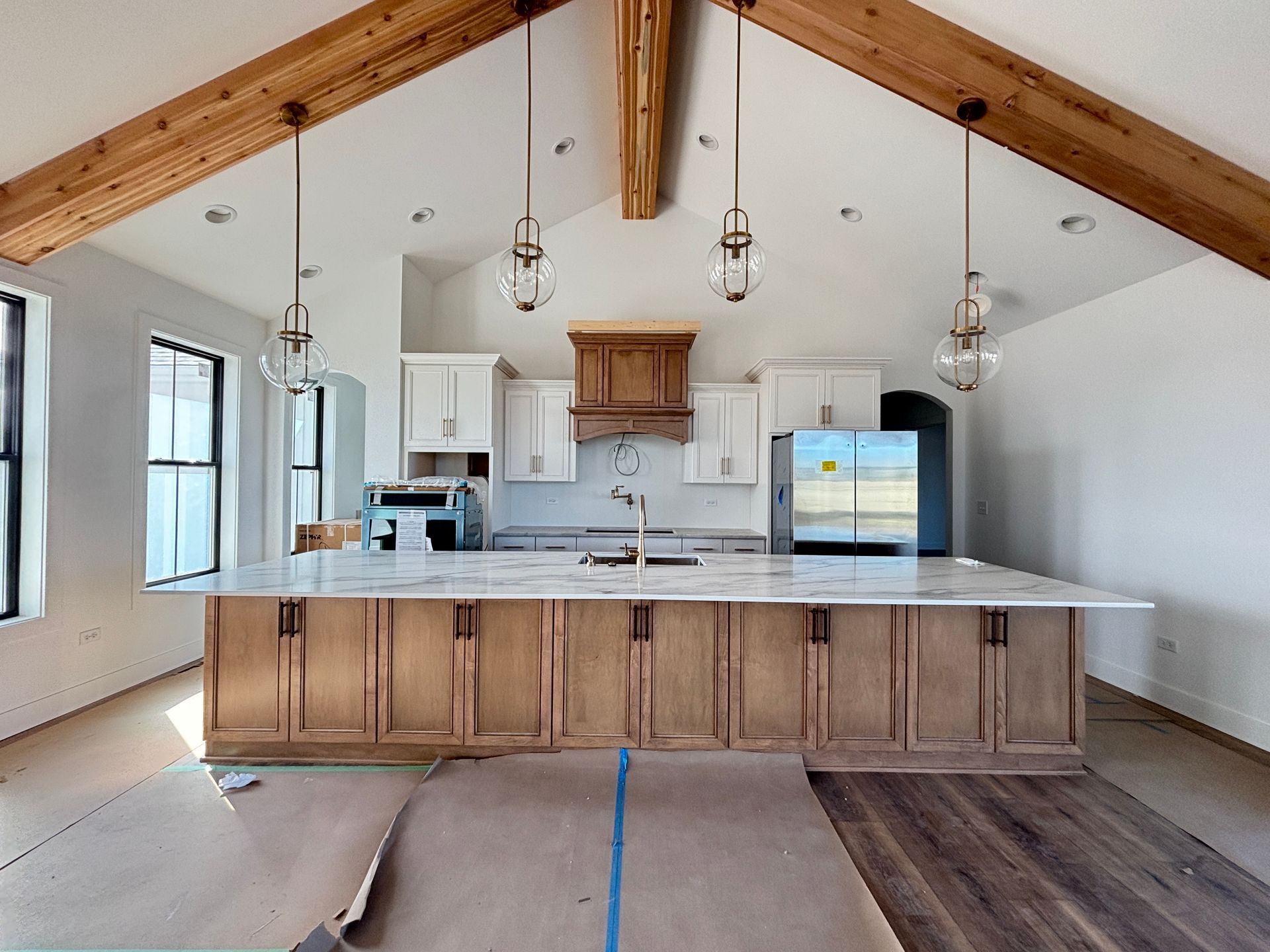 Bright kitchen with vaulted wood-beam ceiling, island, white cabinets, and stainless-steel refrigerator.
