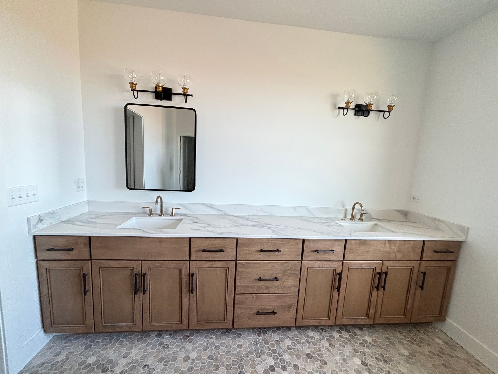Double vanity bathroom with wood cabinets, white marble countertop, and twin mirrors on a light wall