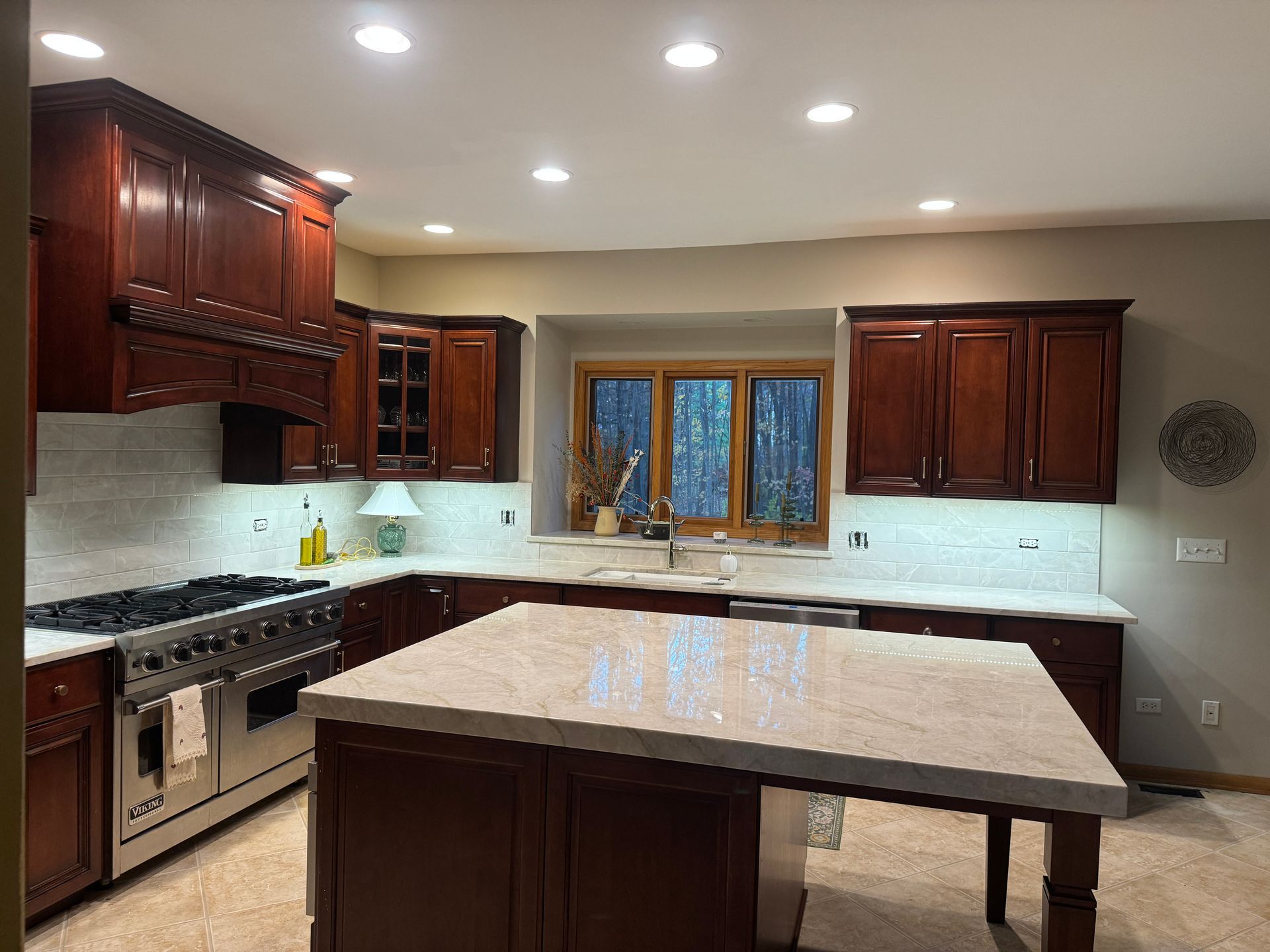 Modern kitchen with dark wood cabinets, white countertops, and a large island under recessed lights