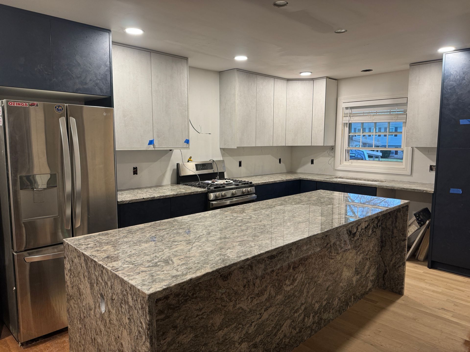 Modern kitchen with granite island, stainless refrigerator, white cabinets, and tiled backsplash