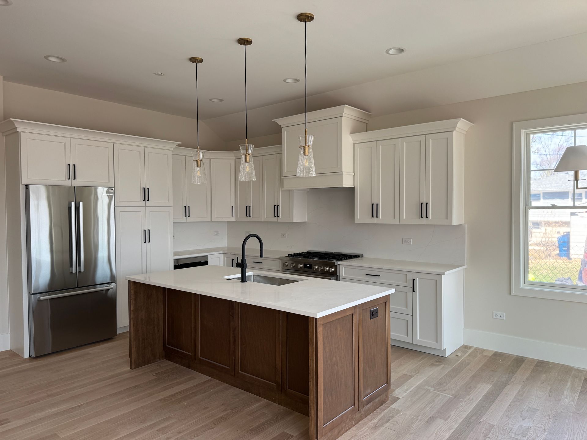 Bright modern kitchen with white cabinets, stainless fridge, and dark wood island with white countertop.