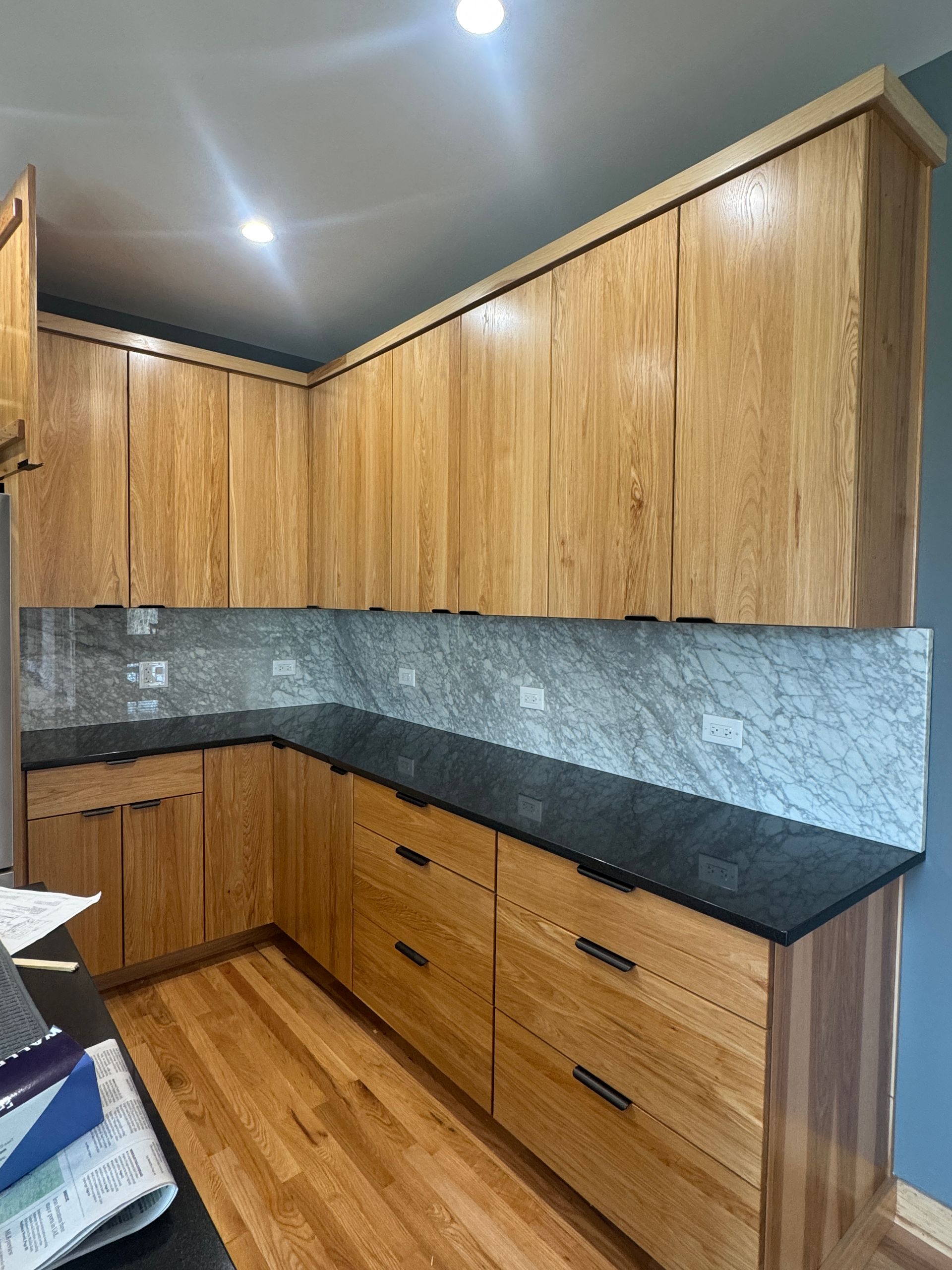 Corner kitchen with wood cabinets, black countertops, gray tile backsplash, and hardwood floor