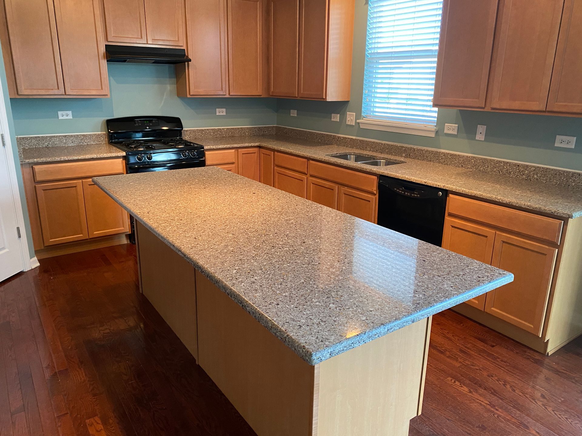 Modern kitchen with wooden cabinets, granite island, black appliances, and hardwood floors.