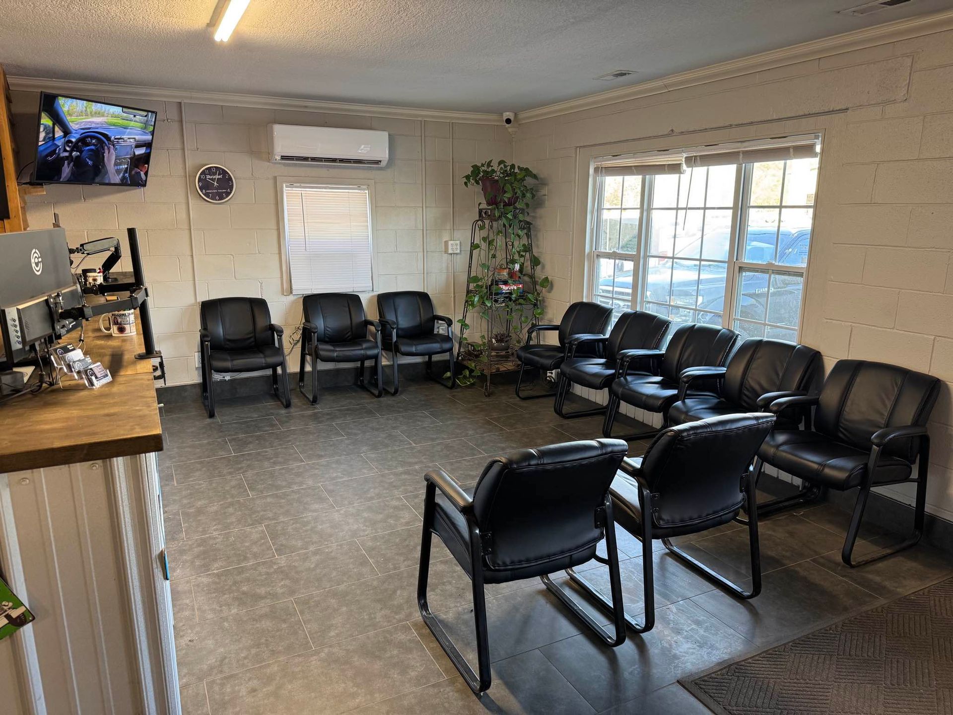 A waiting room with rows of black chairs, a counter on the left, a television on the wall, and a large window.