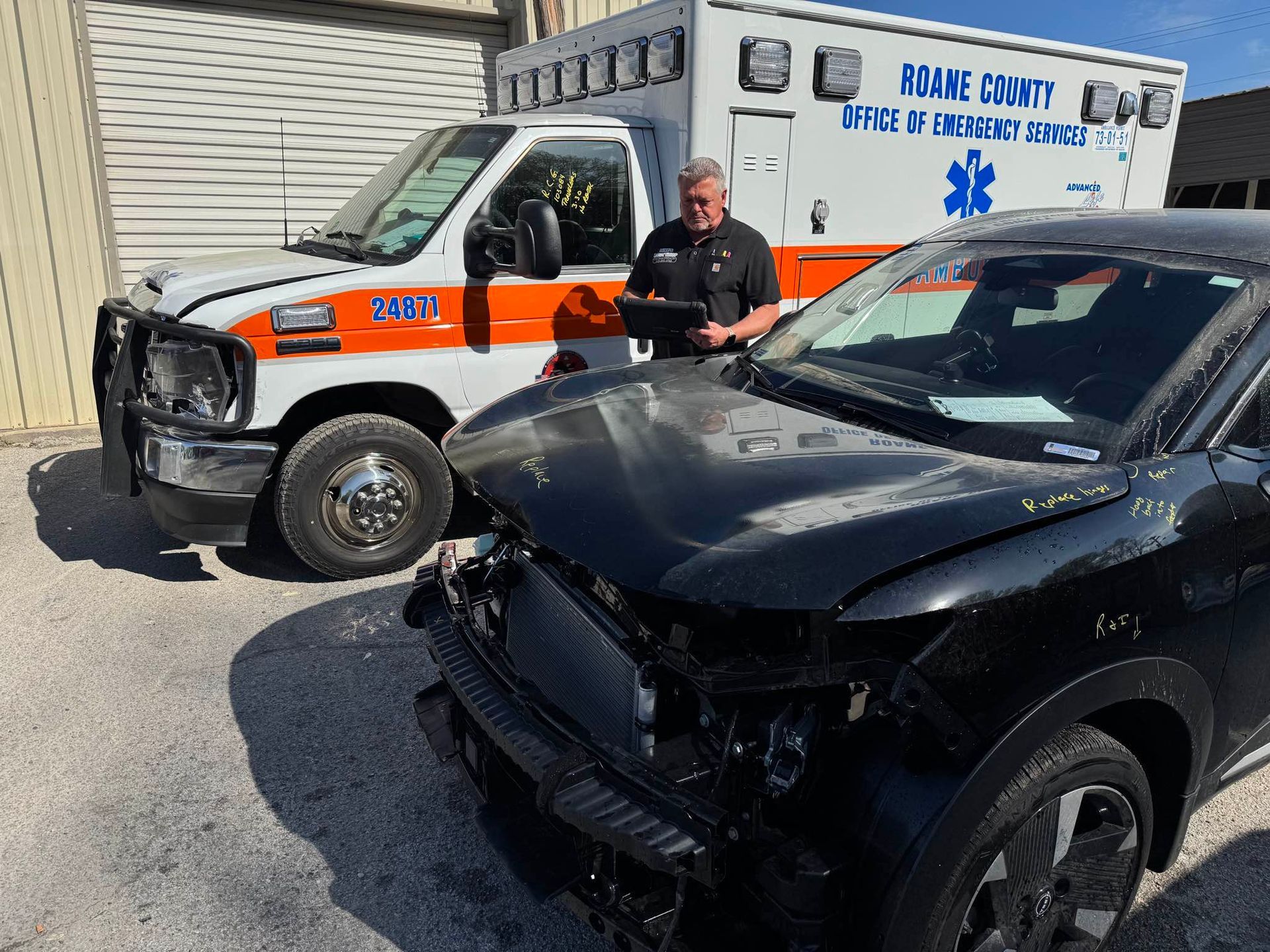 A dark gray SUV parked in an auto repair shop with a detached bumper on a stand near a blue toolbox.