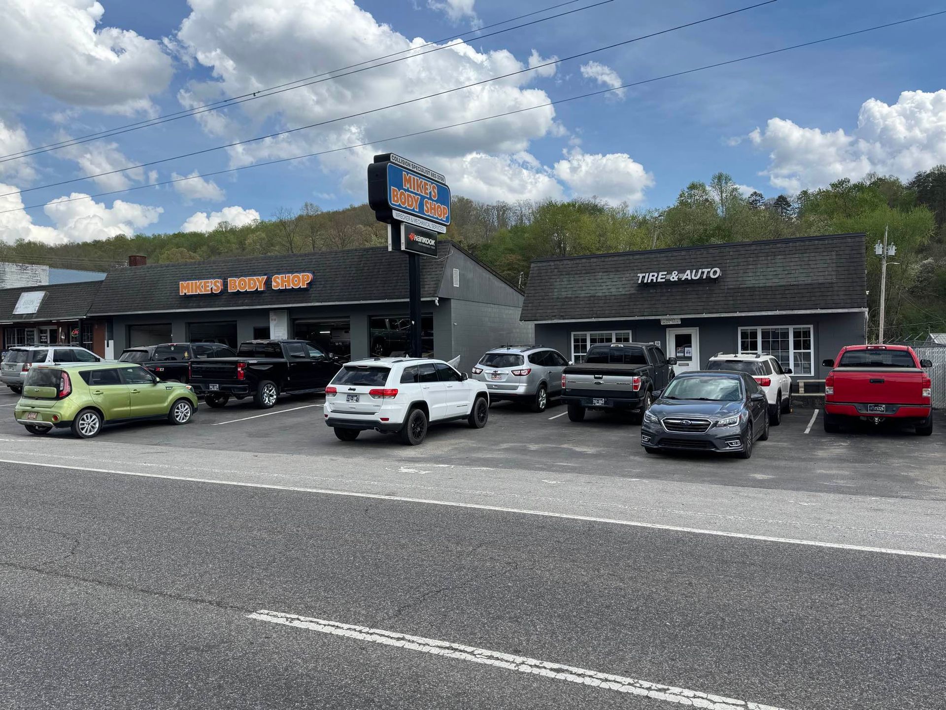 A row of businesses with cars parked in a lot under a bright, cloudy sky.