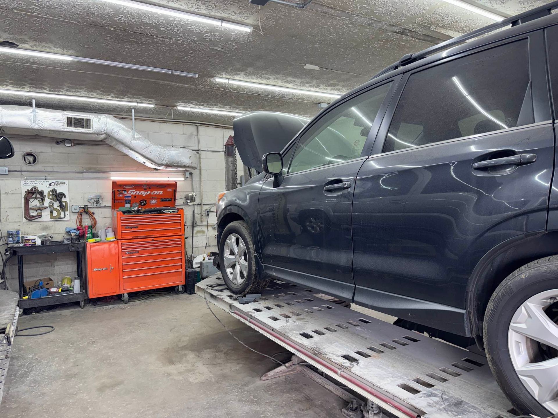 A dark SUV parked on a vehicle lift in a garage with an orange tool chest against the back wall.