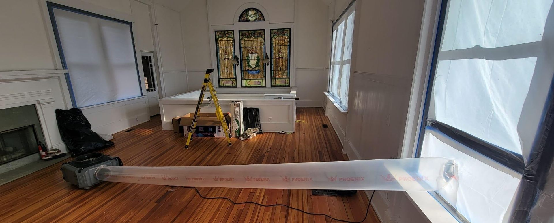 Empty living room with hardwood floors, white walls, a hutch, chairs, and a long white strip on the floor