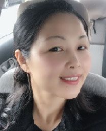 A person with dark hair smiling at the camera while sitting in the front seat of a car.