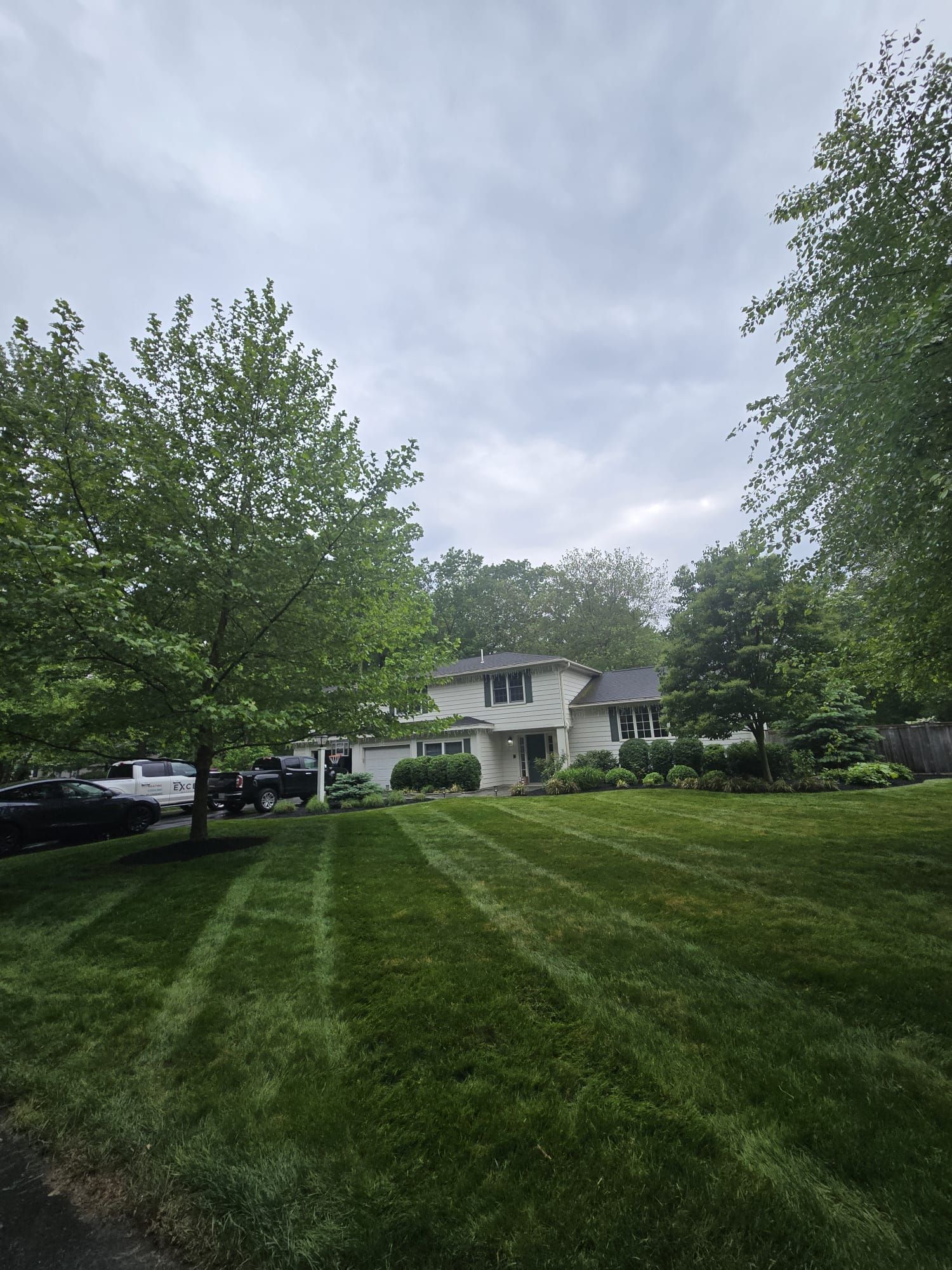 A two-story white house with dark shutters sits behind a large, well-manicured lawn with visible mowing stripes.