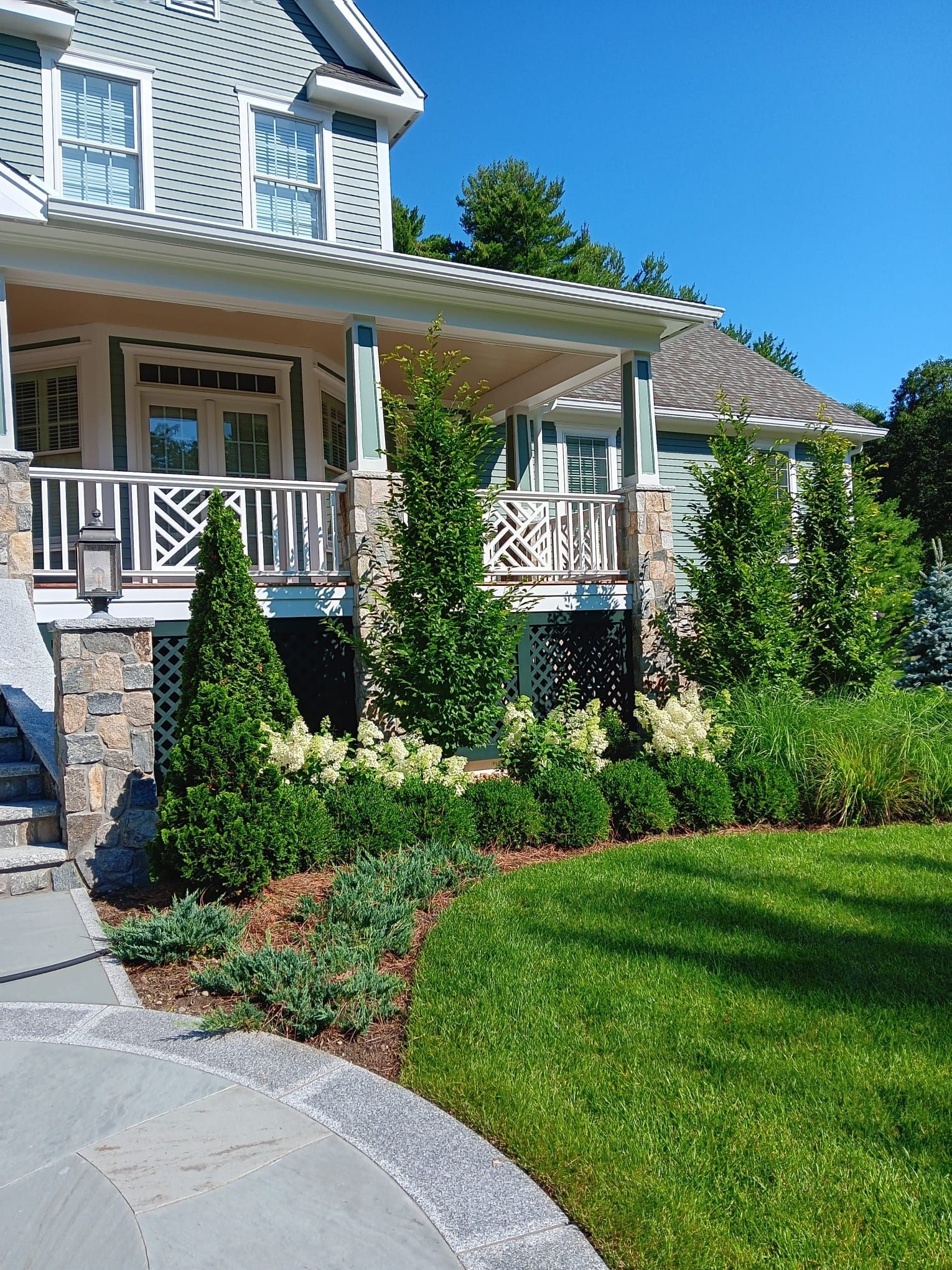 A two-story blue-gray house with a stone-columned front porch and a manicured lawn with structured landscaping.