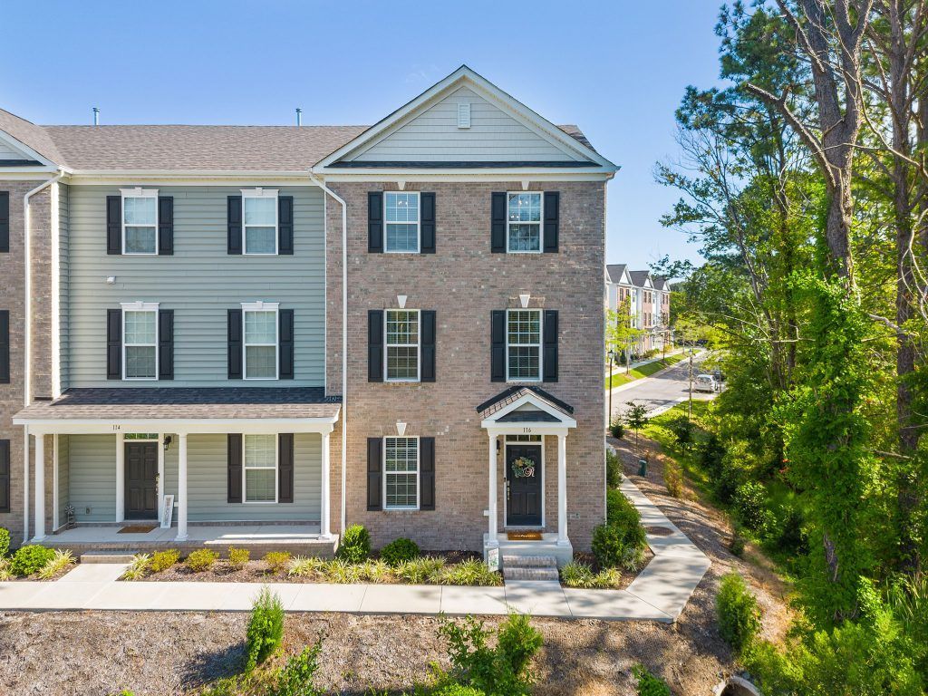 Three-story townhouse exterior with gray siding, brick facade, and front porch on a sunny day