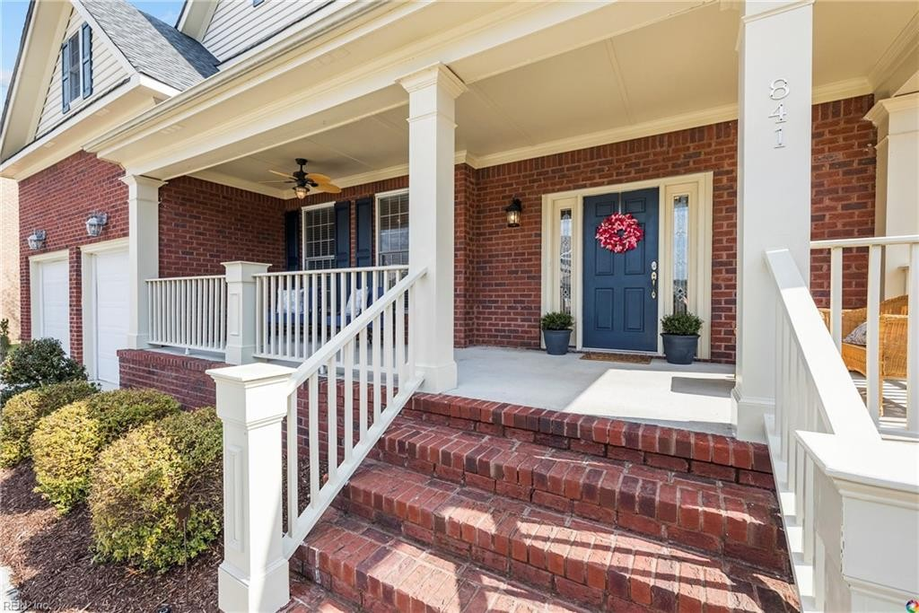 Brick house front porch with white railings, red steps, and blue double doors with a wreath