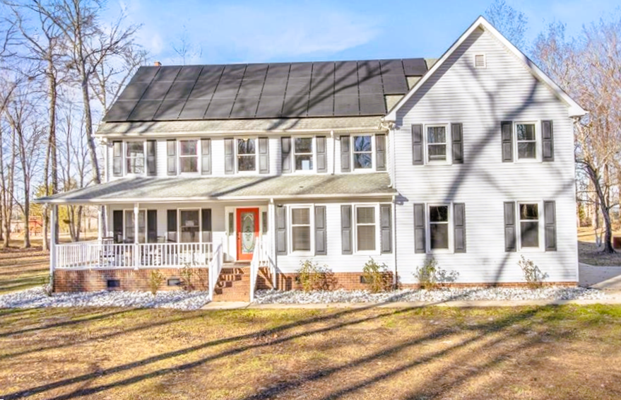 Large white two-story house with black roof, front porch, and autumn trees in the yard