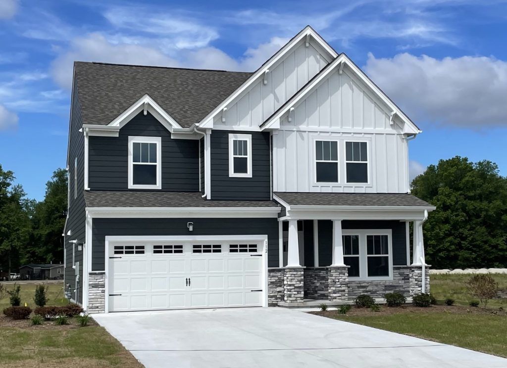 Two-story gray-and-white suburban house with a double garage and a front porch under a blue sky