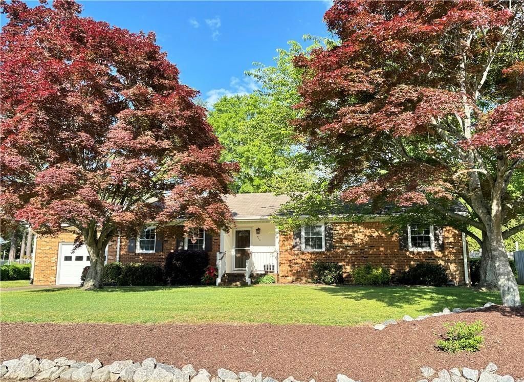 Single-story brick house with red-leafed trees and a manicured front yard