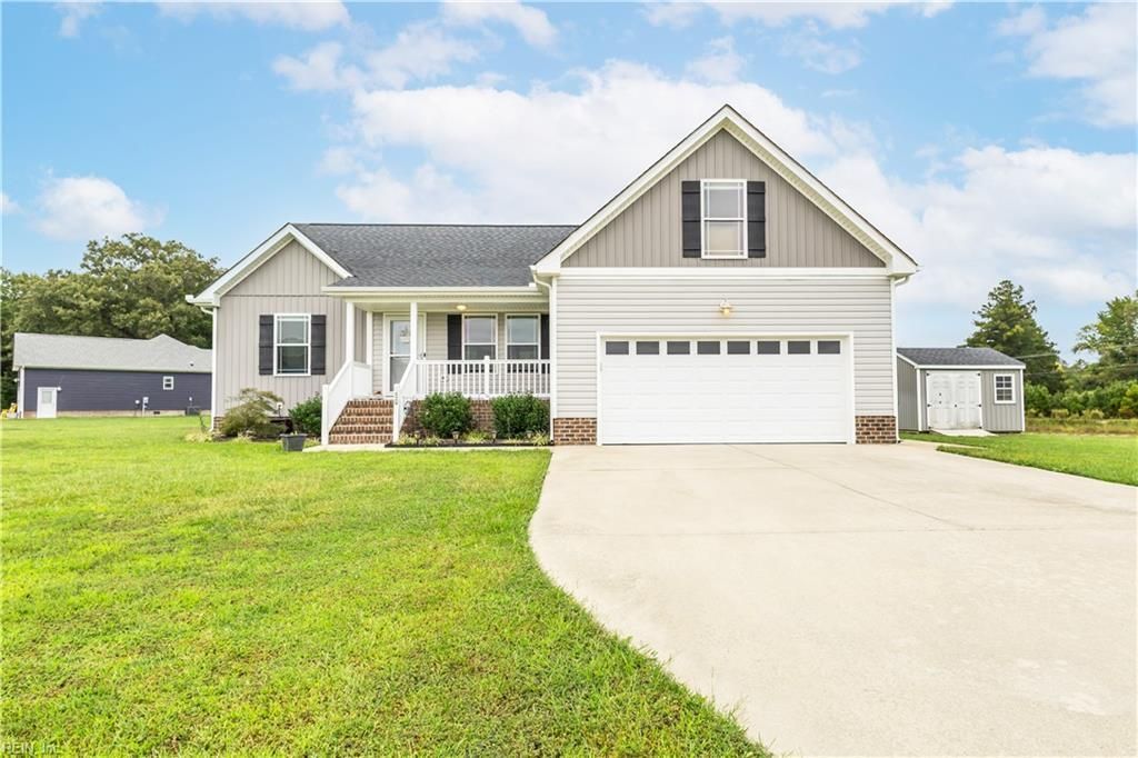 Suburban house with gray siding, white garage, and a curved driveway beside a green lawn
