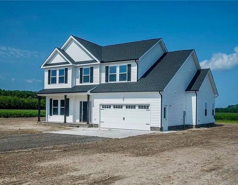 New white two-story house with gray roof and attached garage on a dirt lot under blue sky