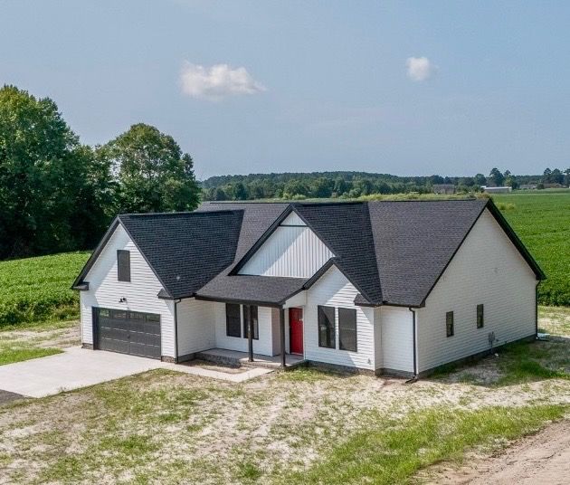 Modern single-story white house with black roof in a rural field, viewed from above