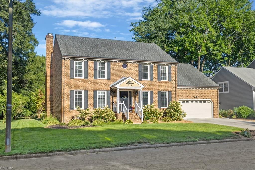 Two-story brick house with white shutters, front porch, and attached garage on a sunny suburban street