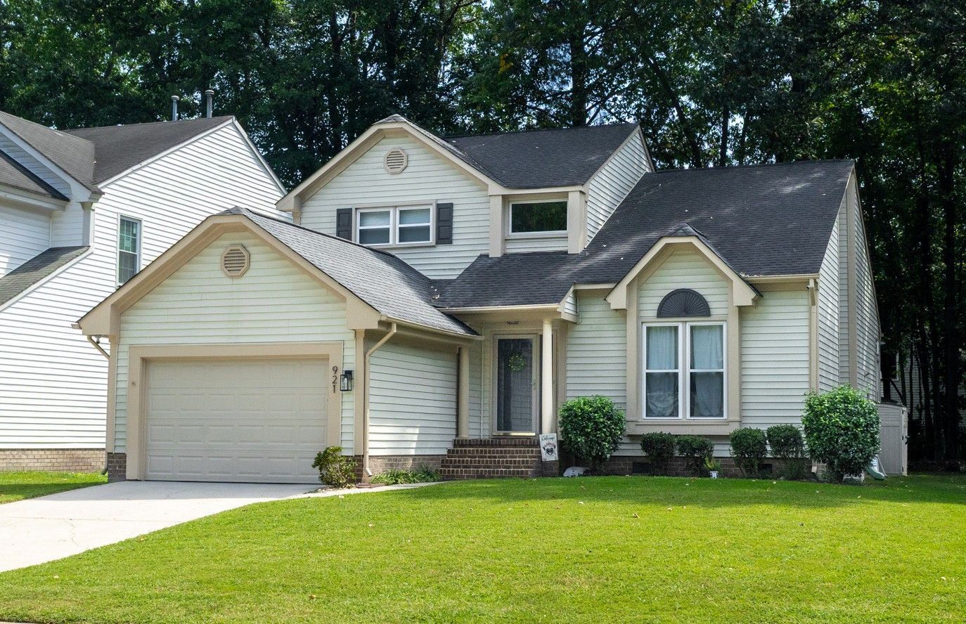 Suburban beige house with attached garage, front porch, and green lawn