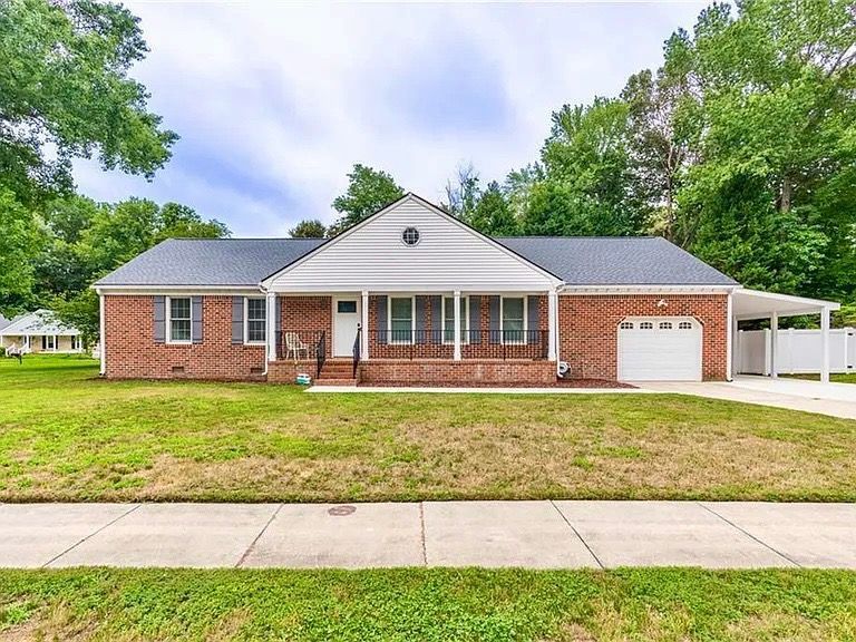 Single-story brick house with a front porch, attached garage, and a driveway beside a lawn.