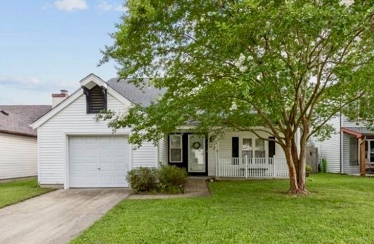 White suburban house with garage, front porch, and large tree on a green lawn