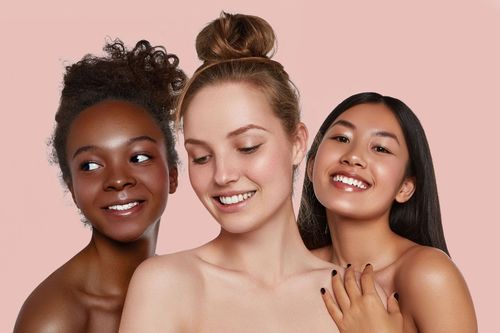 Three smiling people with skincare, posing against a pink background.