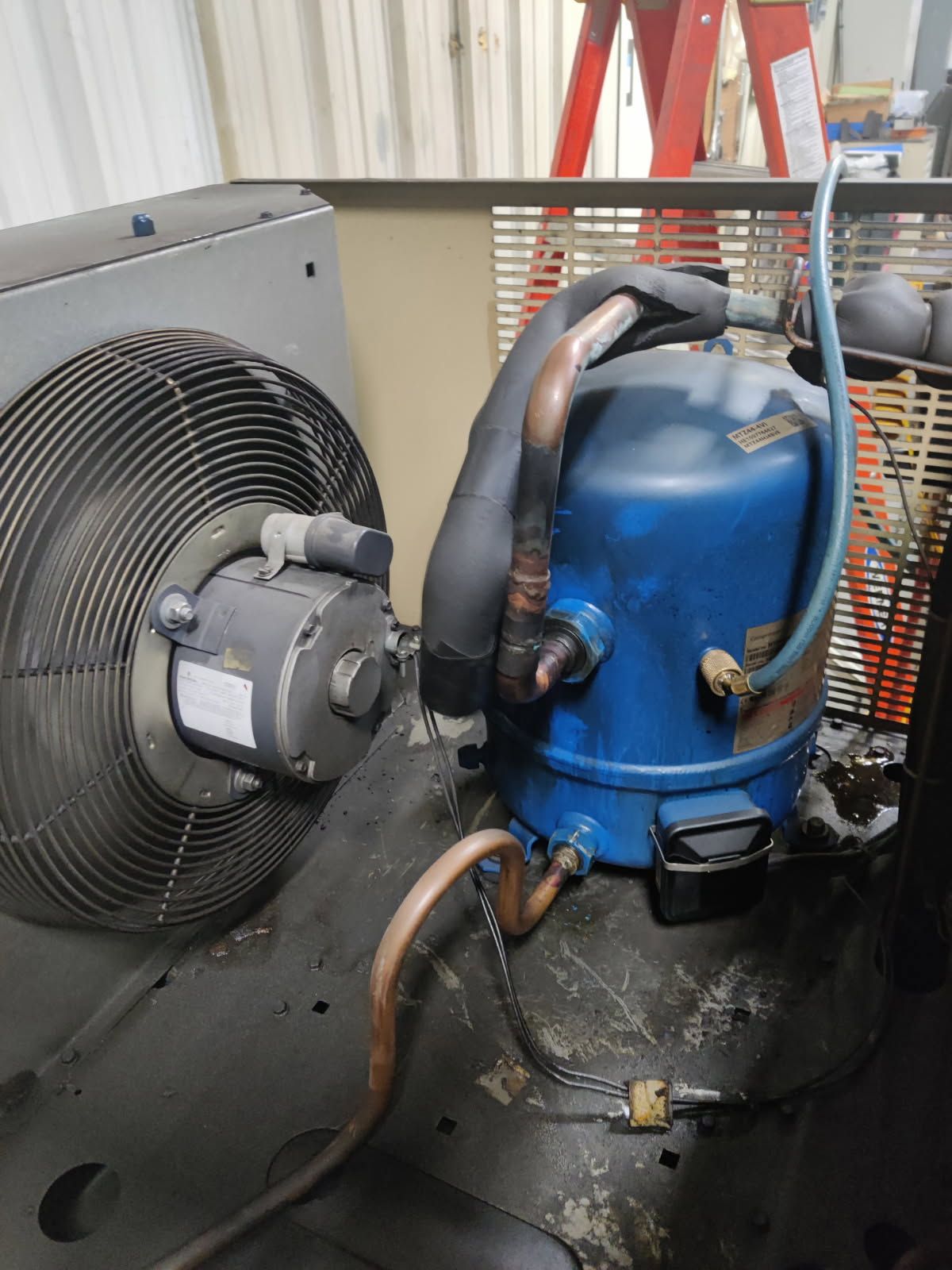 A blue compressor is sitting next to a fan.