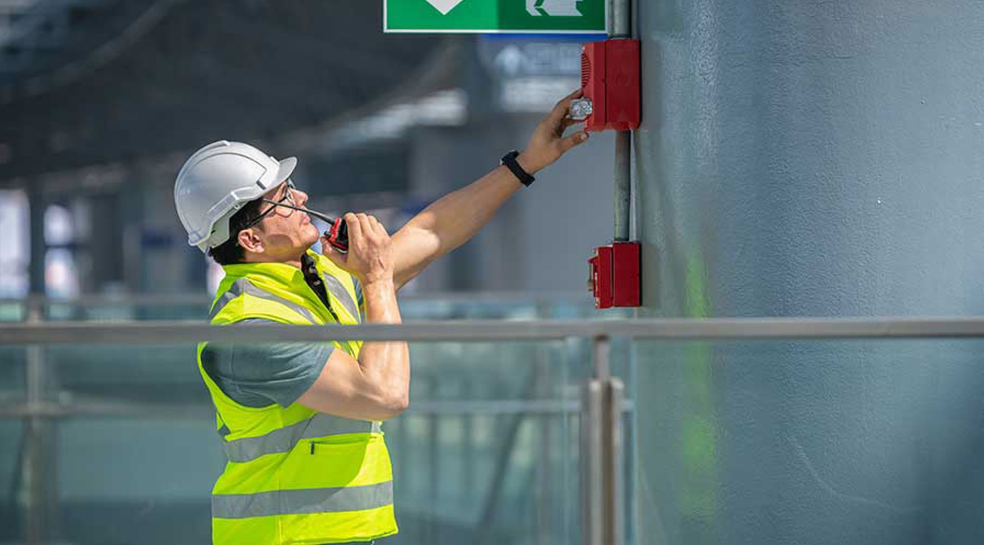 A man is talking on a walkie talkie while working on a fire alarm.