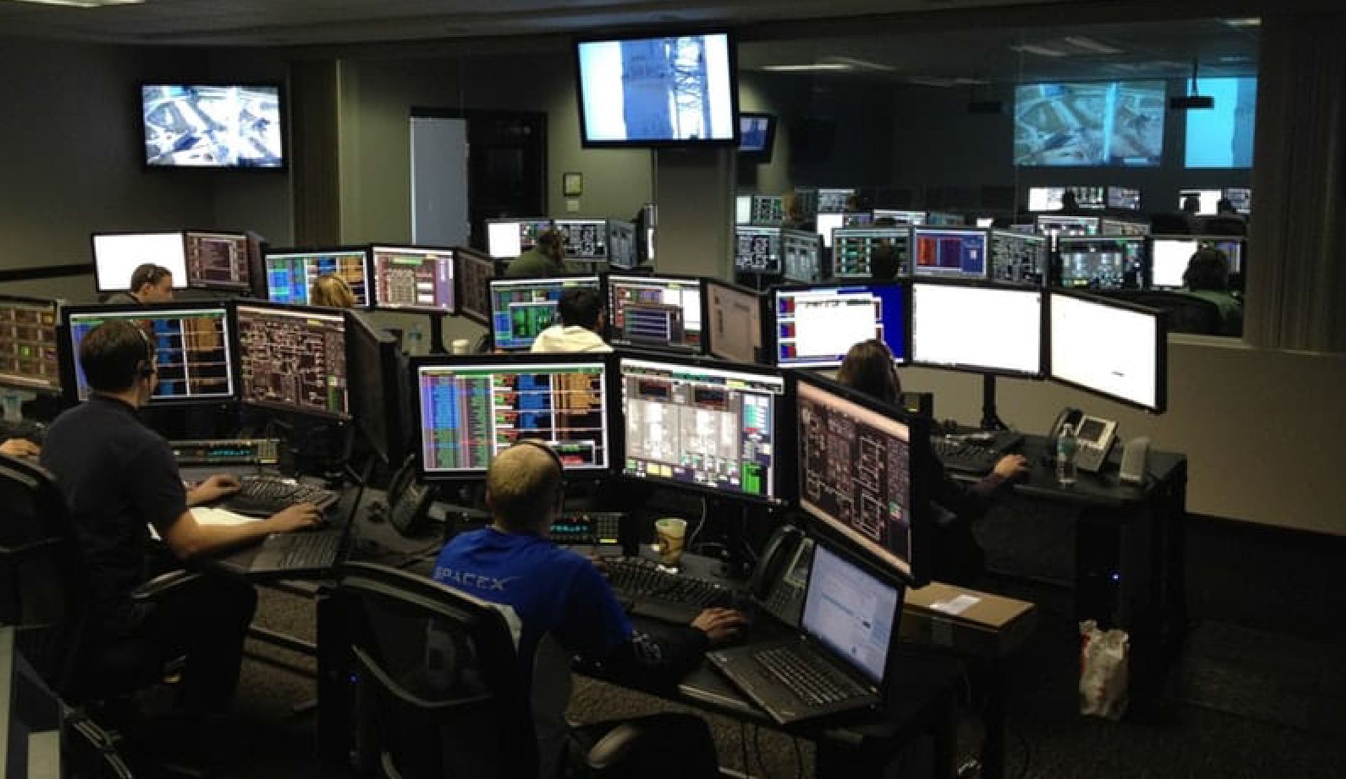 A group of people are sitting in front of computer monitors.